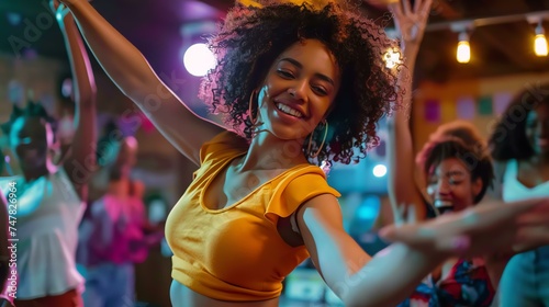 Beautiful young woman with curly hair dancing at a party. She is wearing a yellow top and has a big smile on her face.
