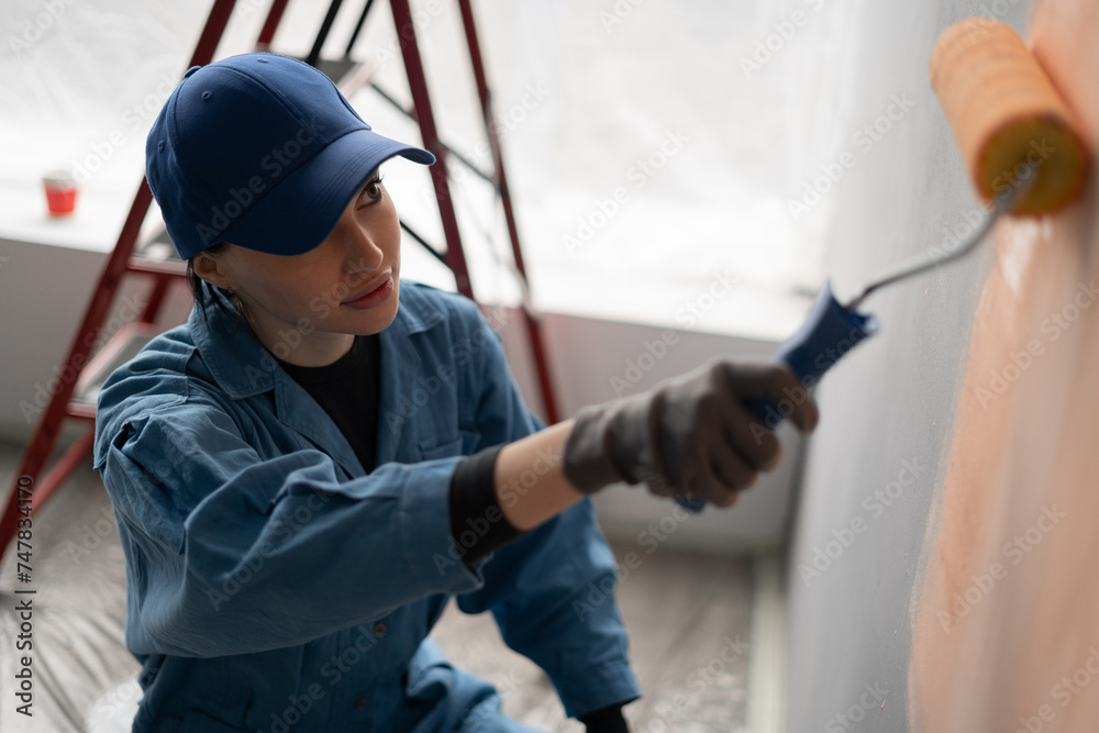above view of painter with cap and gloves painting a wall with paint roller. Home renovation and decoration above view of painter with cap and gloves painting a wall with paint roller. Home renovation and decoration