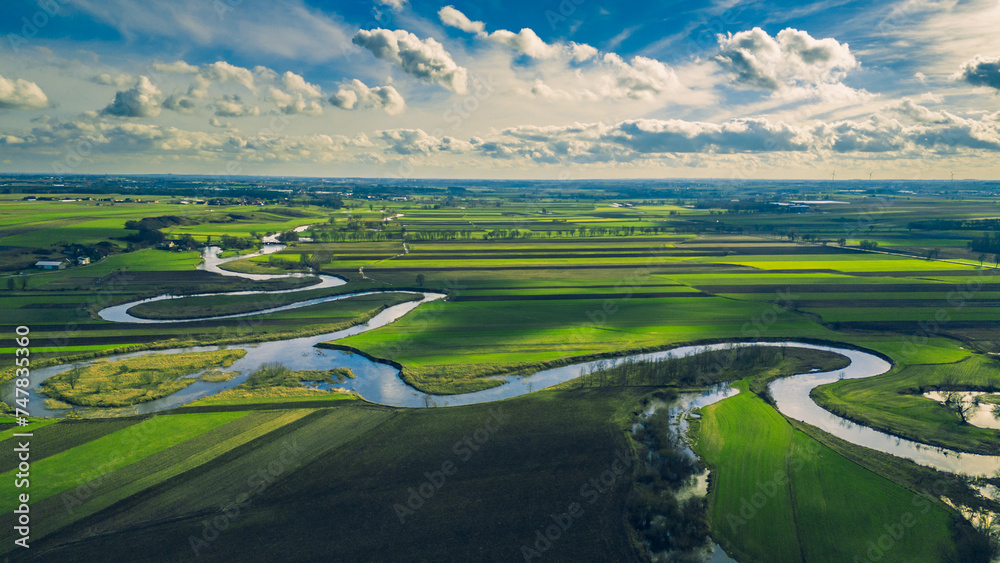 Drone landscape of green fields and meadows, as well as meanders of the Prosna River in Poland on a beautiful sunny spring day with blue sky and clouds Drone landscape of green fields and meadows, as well as meanders of the Prosna River in Poland on a beautiful sunny spring day with blue sky and clouds