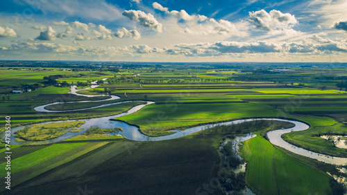 Drone landscape of green fields and meadows, as well as meanders of the Prosna River in Poland on a beautiful sunny spring day with blue sky and clouds