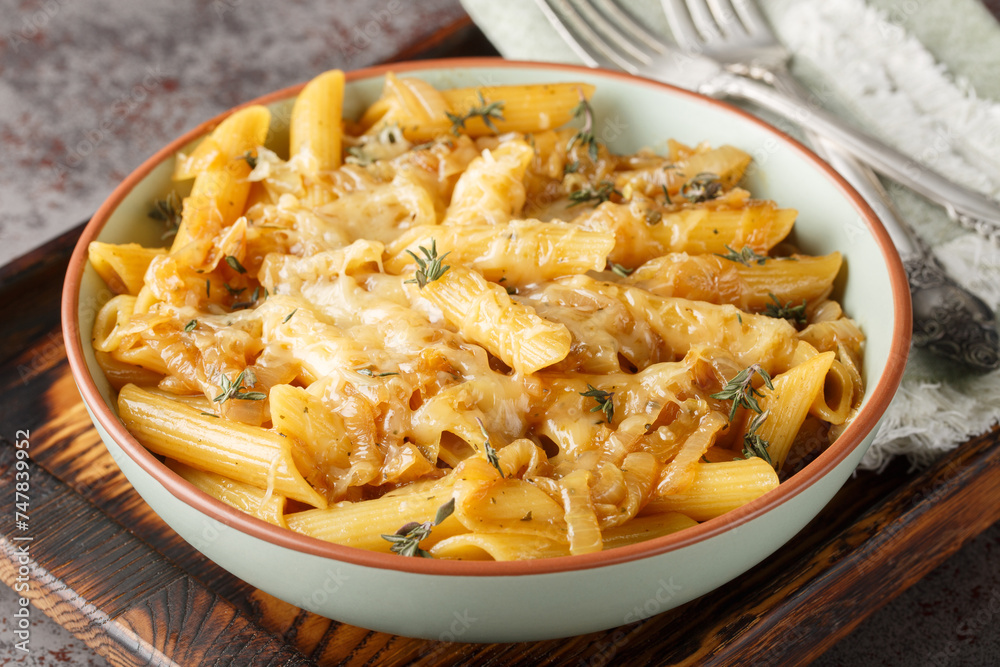 Delicious French onion pasta penne with caramelized onions, fragrant thyme, garlic and gruyere cheese close-up on a bowl on a wooden board. Horizontal