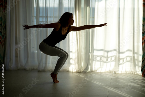 Fototapeta Naklejka Na Ścianę i Meble -  silhouette Beautiful cute sporty woman doing exercise in bright room. on the floor practicing yoga wear tip and leggings. Home mood, lifestyle