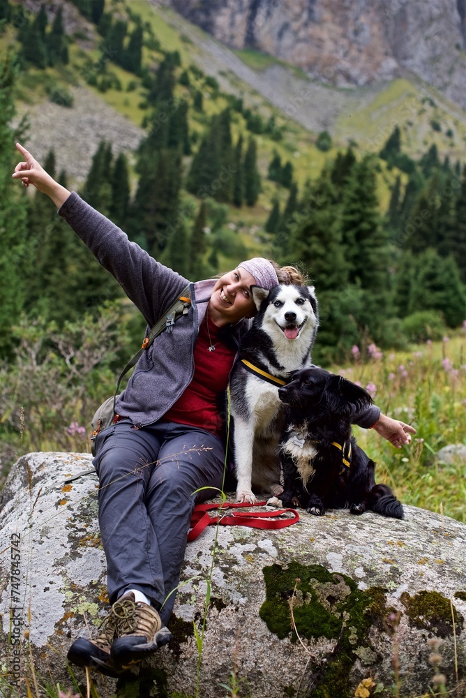 Young girl sitting on the rock next to a black dog and a husky on the mountains hike
