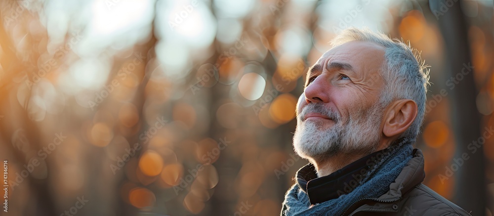 Fototapeta premium An adult man with a beard and jacket is standing outdoors, gazing upwards. He appears contemplative, possibly enjoying the fresh air in a natural setting to promote mental well-being and relaxation.