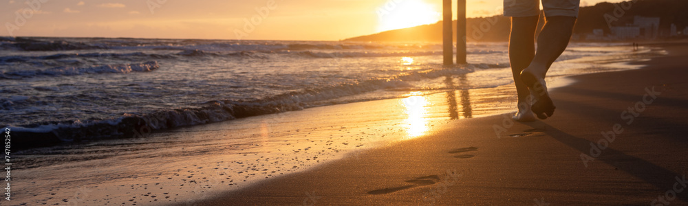 Web banner 4x1. The incoming waves on the sandy beach at sunset. A sunny path. Bare footprints