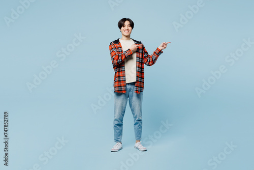 Full body smiling happy young man of Asian ethnicity he wears red hoody casual clothes point index finger aside on area mockup isolated on plain pastel light blue cyan background. Lifestyle concept.