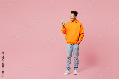 Full body fun young man of African American ethnicity he wear yellow hoody casual clothes hold in hand use mobile cell phone isolated on plain pastel light pink background studio. Lifestyle concept.
