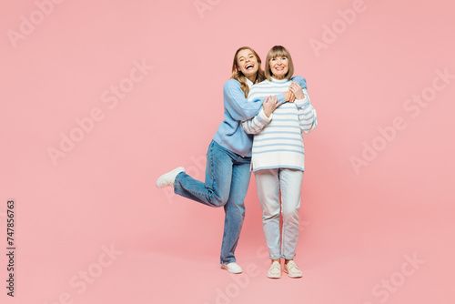 Full body smiling happy elder parent mom with young adult daughter two women together wearing blue casual clothes hug cuddle embrace isolated on plain pastel light pink background. Family day concept.