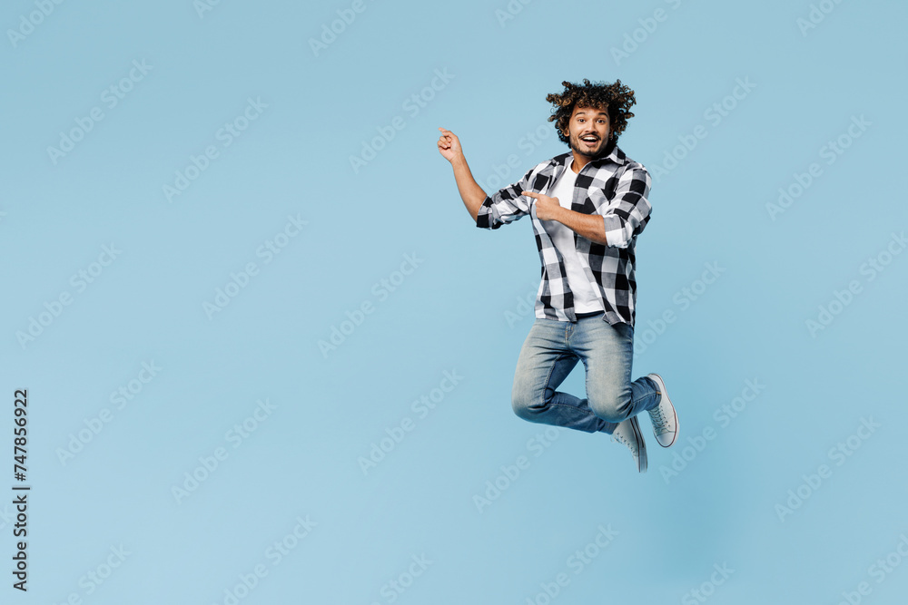 Full body young Indian man wears shirt white t-shirt casual clothes jump high point index finger aside on area isolated on plain pastel light blue cyan background studio portrait. Lifestyle concept Full body young Indian man wears shirt white t-shirt casual clothes jump high point index finger aside on area isolated on plain pastel light blue cyan background studio portrait. Lifestyle concept