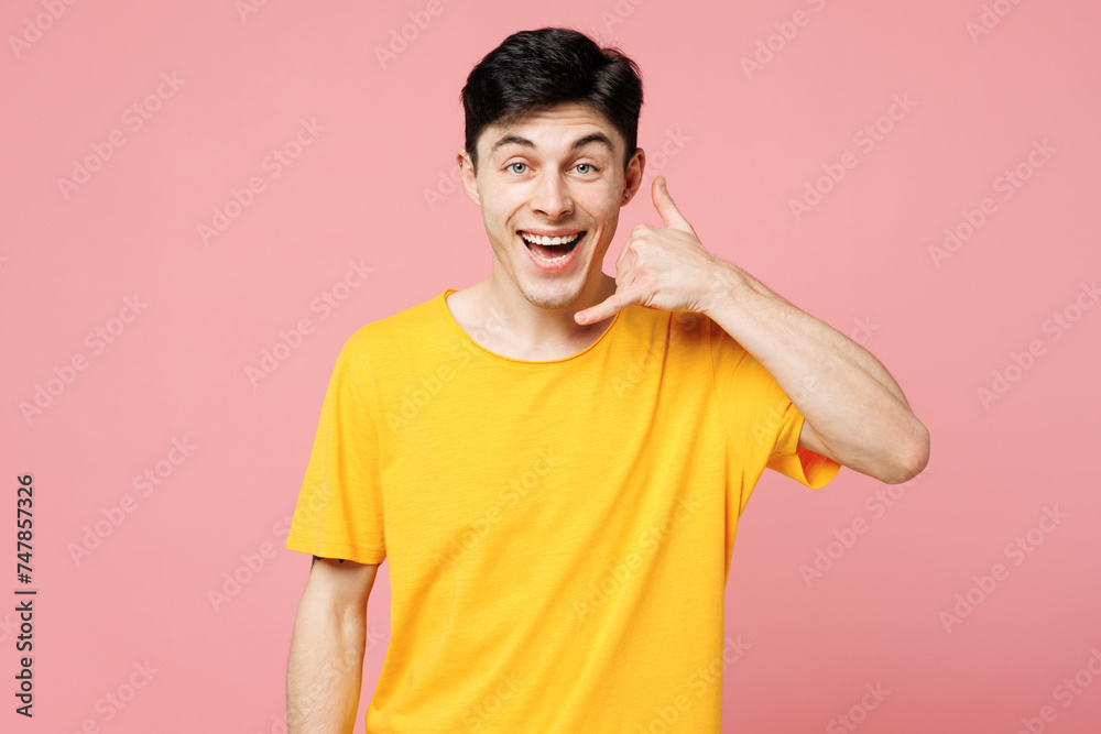 Young surprised happy Caucasian man he wears yellow t-shirt casual clothes doing phone gesture like says call me back isolated on plain pastel light pink background studio portrait. Lifestyle concept. Young surprised happy Caucasian man he wears yellow t-shirt casual clothes doing phone gesture like says call me back isolated on plain pastel light pink background studio portrait. Lifestyle concept.