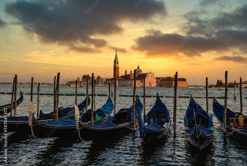 many gondolas parked on the water as the sun goes down