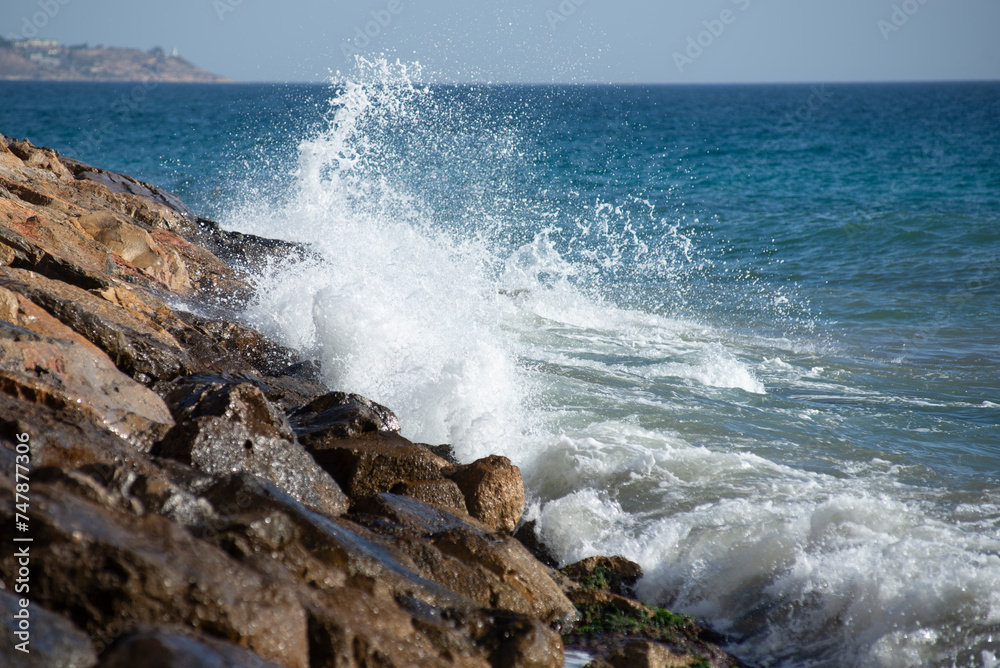 Waves crashing on the rocks in the mediterranean sea at sunset, turquoise water, white foam