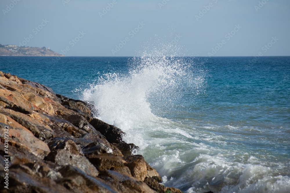 Waves crashing on the rocks in the mediterranean sea at sunset, turquoise water, white foam