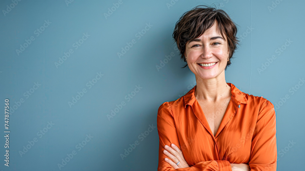 Confident mature woman smiling in orange blouse against a blue background, exuding positivity. Confident mature woman smiling in orange blouse against a blue background, exuding positivity.