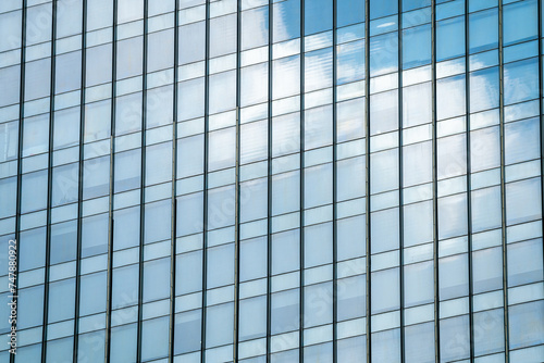 windows of modern office building exterior reflects cloudy sky.