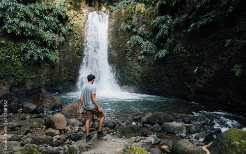 Male tourist on the stones in the rainforest. Young handsome man with a hike in a tropical thicket near a waterfalls from the Azores - Salto do Prego photo