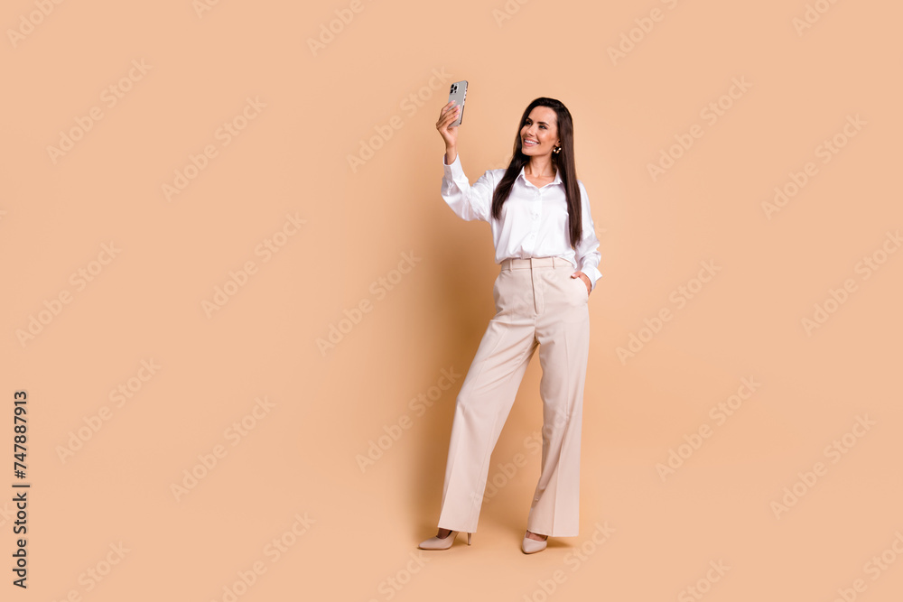 Full length portrait of pretty lovely classy person hold smart phone take selfie empty space isolated on beige color background Full length portrait of pretty lovely classy person hold smart phone take selfie empty space isolated on beige color background