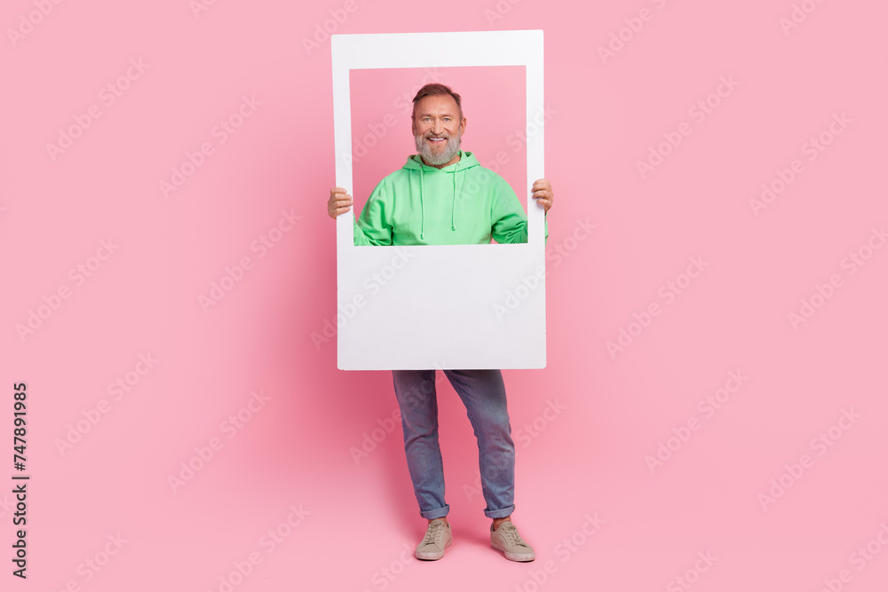 Full length photo of handsome senior man hold instant photo frame dressed stylish green garment isolated on pink color background Full length photo of handsome senior man hold instant photo frame dressed stylish green garment isolated on pink color background