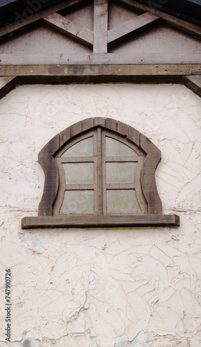 An oddly shaped window and wooden parts of the roof structure in a historic building wall