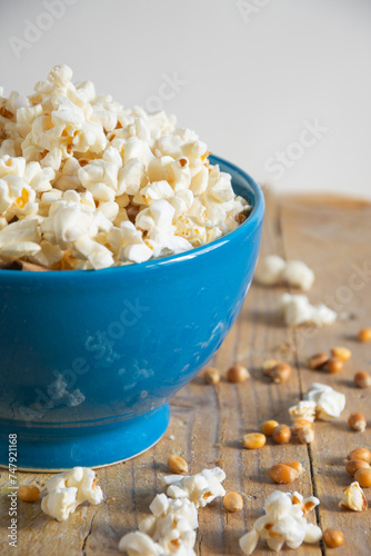Top view of blue bowl with fresh popcorn on rustic wooden table, white background, vertical with copy space