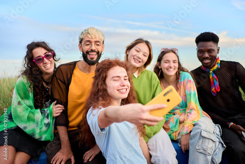 Multi-ethnic group smiling generation z boys and girls taking selfie outdoors. Happy lifestyle concept of friendship in multicultural young people having fun day together. Partners enjoying weekend. 
