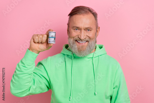Photo of cheerful good mood man wear green sweatshirt rising dollars roll isolated pink color background
