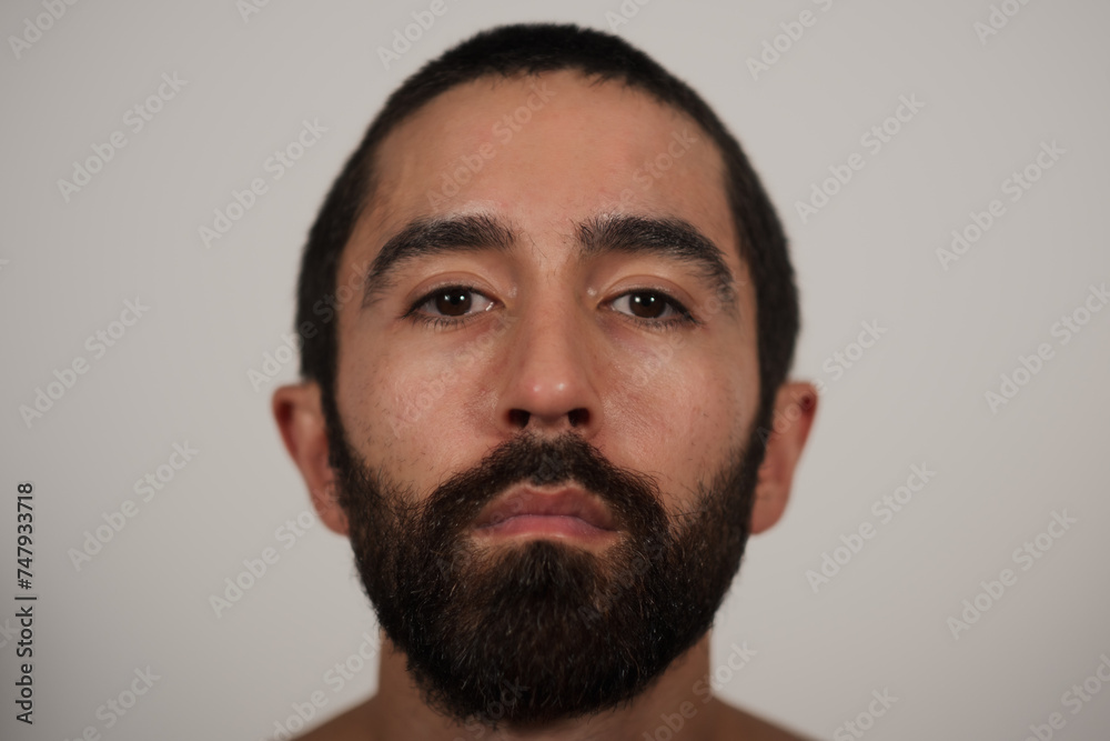 A studio portrait of a multiracial Jewish, Asian, and White man looking neutrally at the camera. His blank expression and shirtless pose highlight his strong eyebrows, dark beard, and dark hair. A studio portrait of a multiracial Jewish, Asian, and White man looking neutrally at the camera. His blank expression and shirtless pose highlight his strong eyebrows, dark beard, and dark hair.
