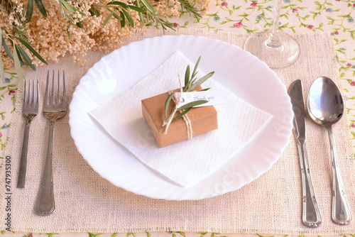 Wedding place setting decoration guest gift brown craft favor box with jute ribbon olive leaves on white plate, burlap table mat and floral cloth, spring summer autumn fall ceremony, banquet, party