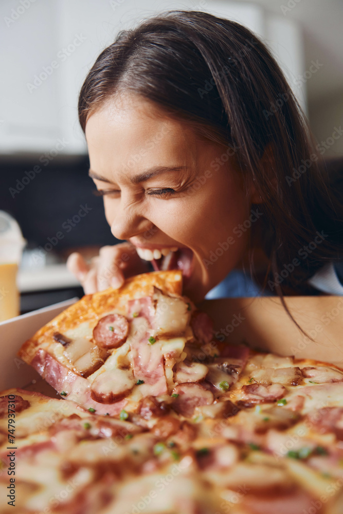 Woman eating pizza with open mouth and drink in front of her in a casual setting Woman eating pizza with open mouth and drink in front of her in a casual setting