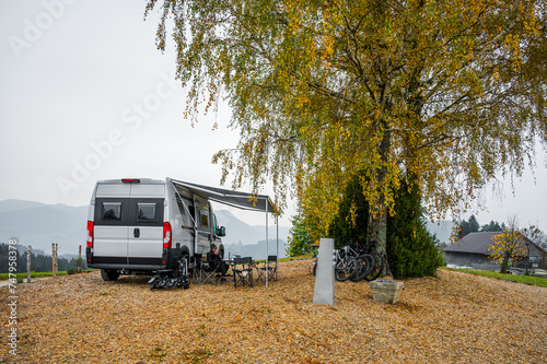 Campervan or motorhome parked in the countryside nature. Woman is drinking coffee in front of camper van motor home RV, parked under the trees when exploring the countryside nature of Slovenia, Europe