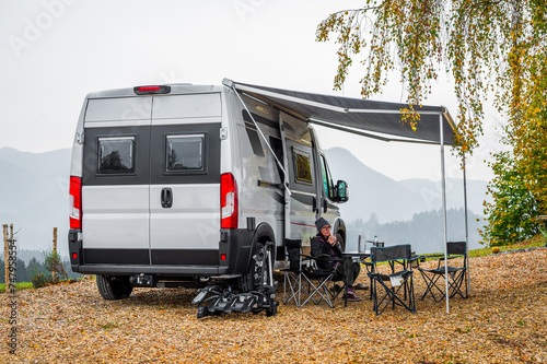 Campervan or motorhome parked in the countryside nature. Woman is drinking coffee in front of camper van motor home RV, parked under the trees when exploring the countryside nature of Slovenia, Europe
