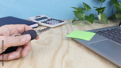 Hand holding car key on desk background with props and green climbing plant. series of photos.