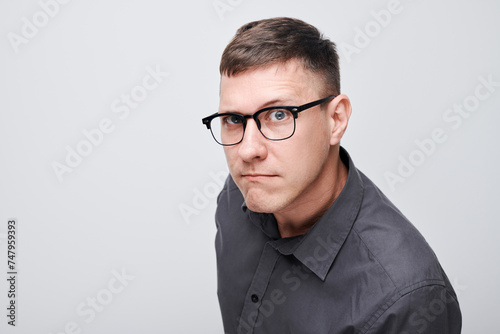 Portrait of a serious man with glasses wearing a gray shirt against a light background. © amixstudio