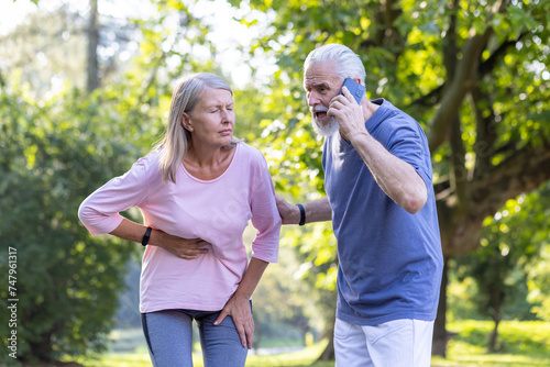 Wallpaper Mural Elderly woman feeling abdominal pain while exercising, concerned man with beard making emergency call in park. Torontodigital.ca