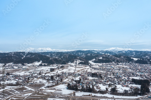 ドローン写真：晴れた日の冬の田舎町と雪山