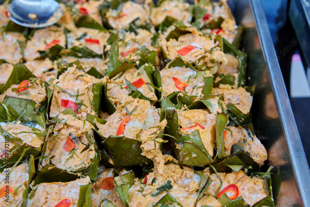 Fototapeta premium Steamed fish with curry paste wrapped with banana leaf in plate on table