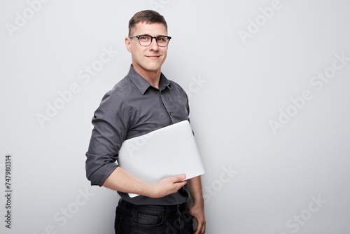 Confident young man in glasses holding a laptop against a white background with copy space.
