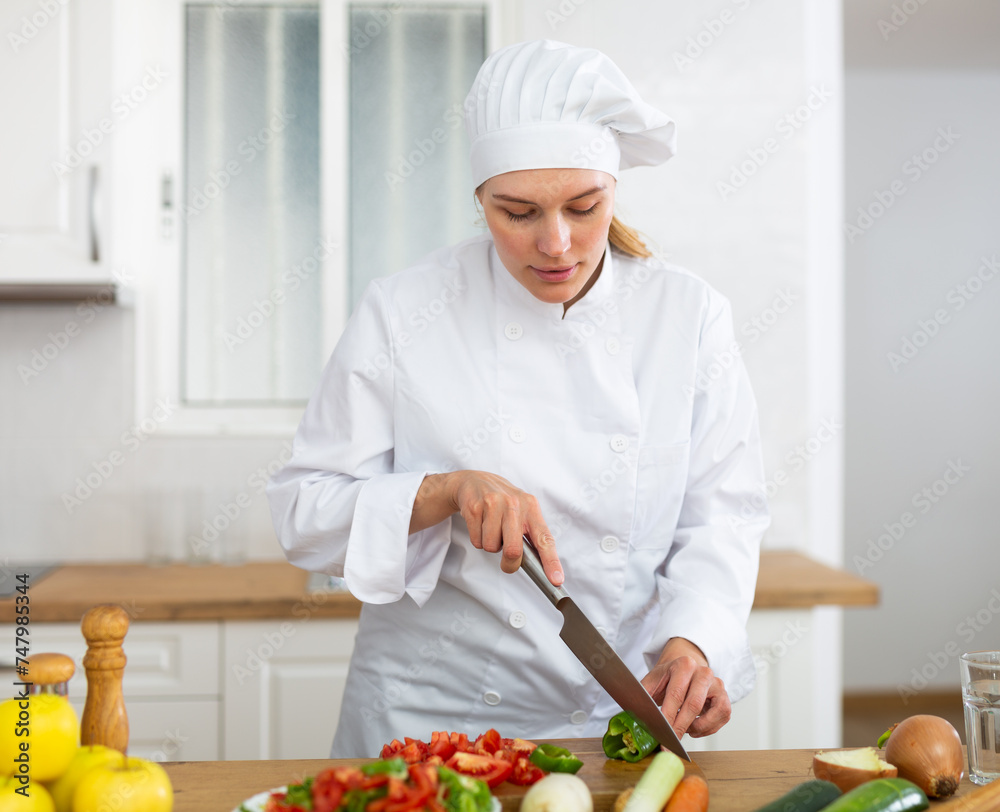 Smiling female chef in white uniform preparing vegetable salad in private kitchen Smiling female chef in white uniform preparing vegetable salad in private kitchen