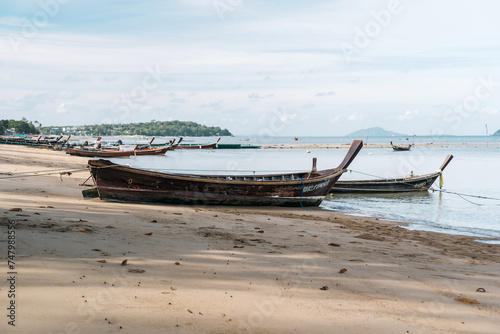A cluster of watercraft including boats made of wood are resting on the beach  close to the water under the vast sky adorned with clouds  creating a picturesque scene at the fluid horizon.