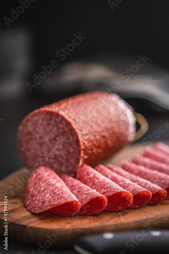 Sliced smoked salami sausages on cutting board on black table. photo