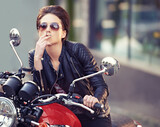 Motorcycle, leather and biker in city with cigarette for travel, or road trip as rebel. Fashion, street and woman smoker with attitude on classic or vintage bike for transportation or journey
