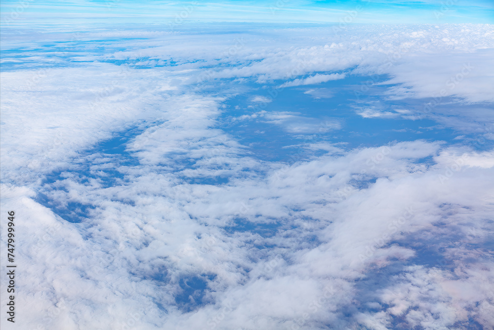 Blue sky with white clouds over the Earth as seen through window of an aircraft