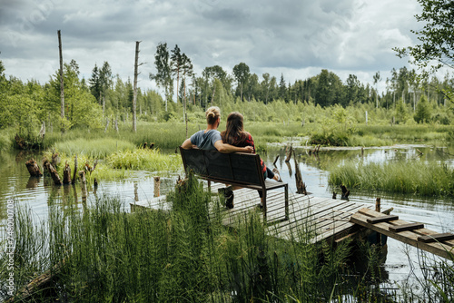 couple with dog sitting on bench in front of stomp lake surrounded by wild forest