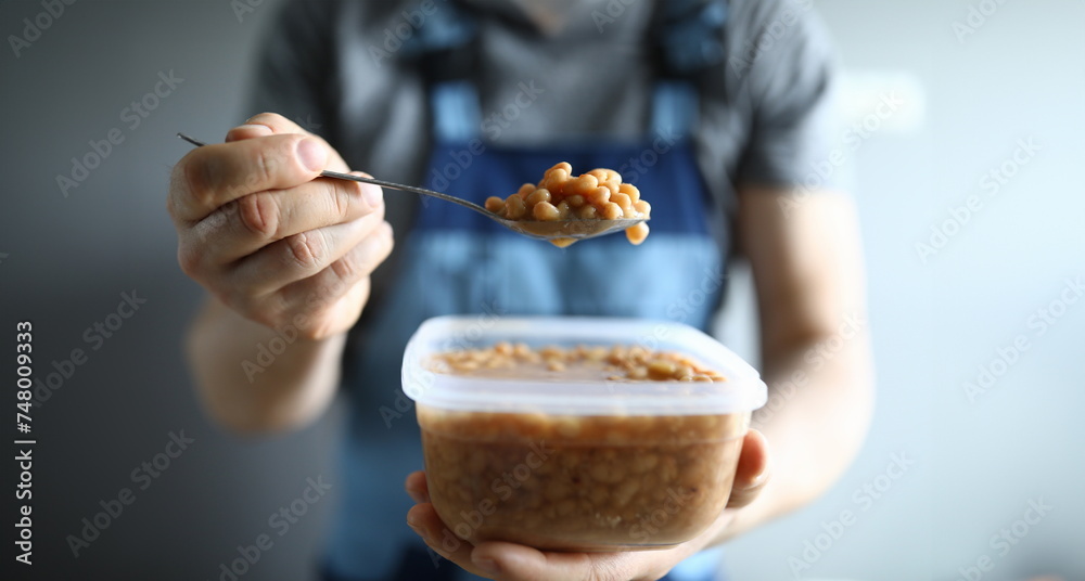 Close-up of service worker holding plastic container with beans lunch. Break from work for snack. Male in working uniform. Renovation and hot meal concept