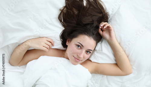 Close-up of wonderful woman after waking up looking at camera with gladness and smile. Beautiful lady relaxing in bedstead after wakeup. Relaxation and vacation concept