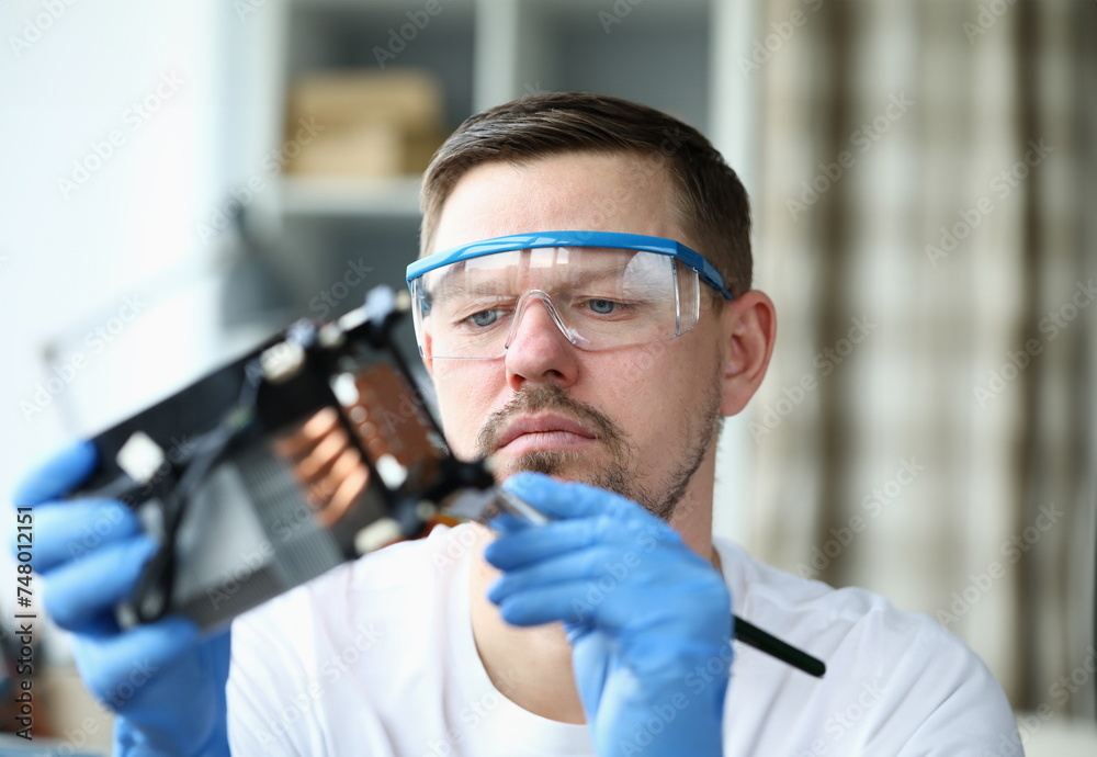 Close-up view of concentrated male in protective eyewear and gloves using forceps for tiny details. Hobby for middle-aged man. Diy and repairman concept Close-up view of concentrated male in protective eyewear and gloves using forceps for tiny details. Hobby for middle-aged man. Diy and repairman concept