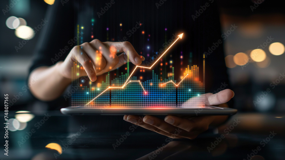 Businessman holding tablet and showing a growing virtual hologram of statistics, graph and chart with arrow up on dark background. Stock market. Business growth, planing and strategy concept. - obrazy, fototapety, plakaty 