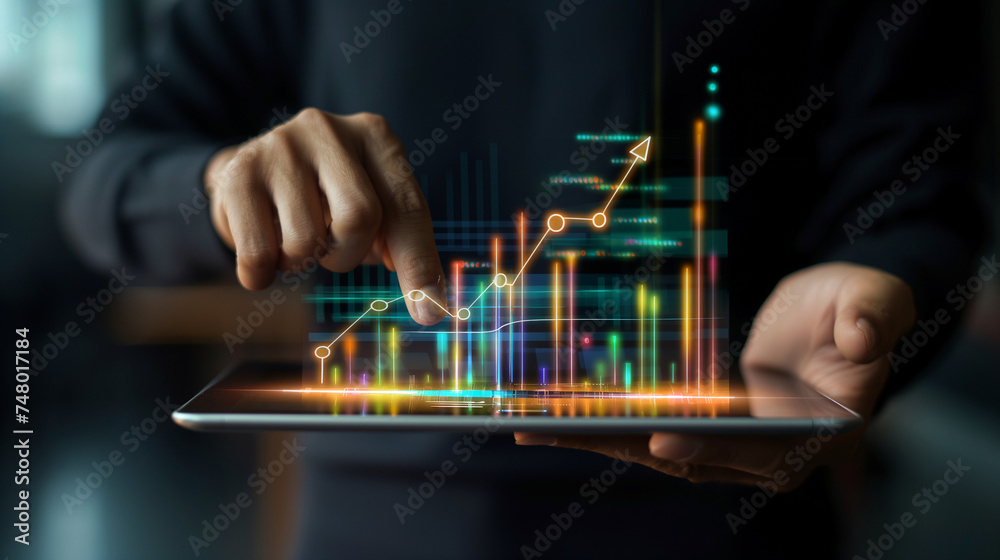 Businessman holding tablet and showing a growing virtual hologram of statistics, graph and chart with arrow up on dark background. Stock market. Business growth, planing and strategy concept. Businessman holding tablet and showing a growing virtual hologram of statistics, graph and chart with arrow up on dark background. Stock market. Business growth, planing and strategy concept.
