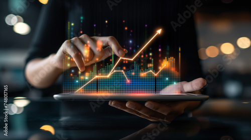 Businessman holding tablet and showing a growing virtual hologram of statistics, graph and chart with arrow up on dark background. Stock market. Business growth, planing and strategy concept.