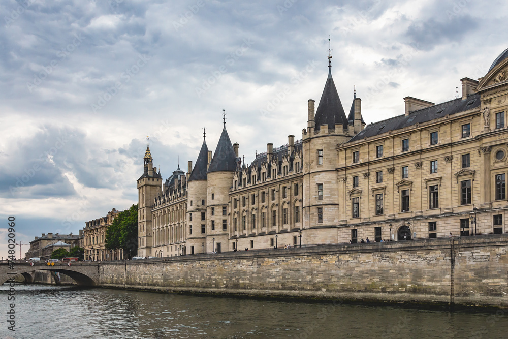 Conciergerie palace and prison on the Ile de la Cite. View from Seine river. Cloudy sky at background. Paris, France